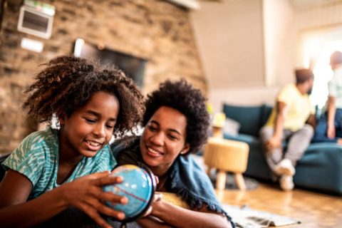 Happy African American girl looking at glove with mother. Planning to travel together / studying.
